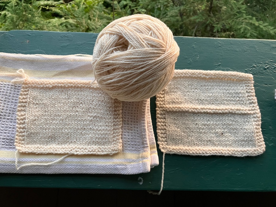 Cream wool swatches and ball of yarn on dark green porch railing